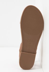 Semelle d'une chaussure marron avec une semelle texturée, taille 4/37, marque "New Look", fabriquée en Chine, reposant contre une surface blanche.