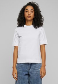 Hvit kortermet t-skjorte med rund hals, laget av myk bomull, med en jevn tekstur og en avslappet passform. Kombinert med blå jeans.