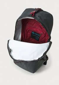 Grauer Rucksack mit einem schlanken Design, ausgestattet mit einem weißen Innenfutter und einer roten Innentasche. Reißverschlussöffnung oben.