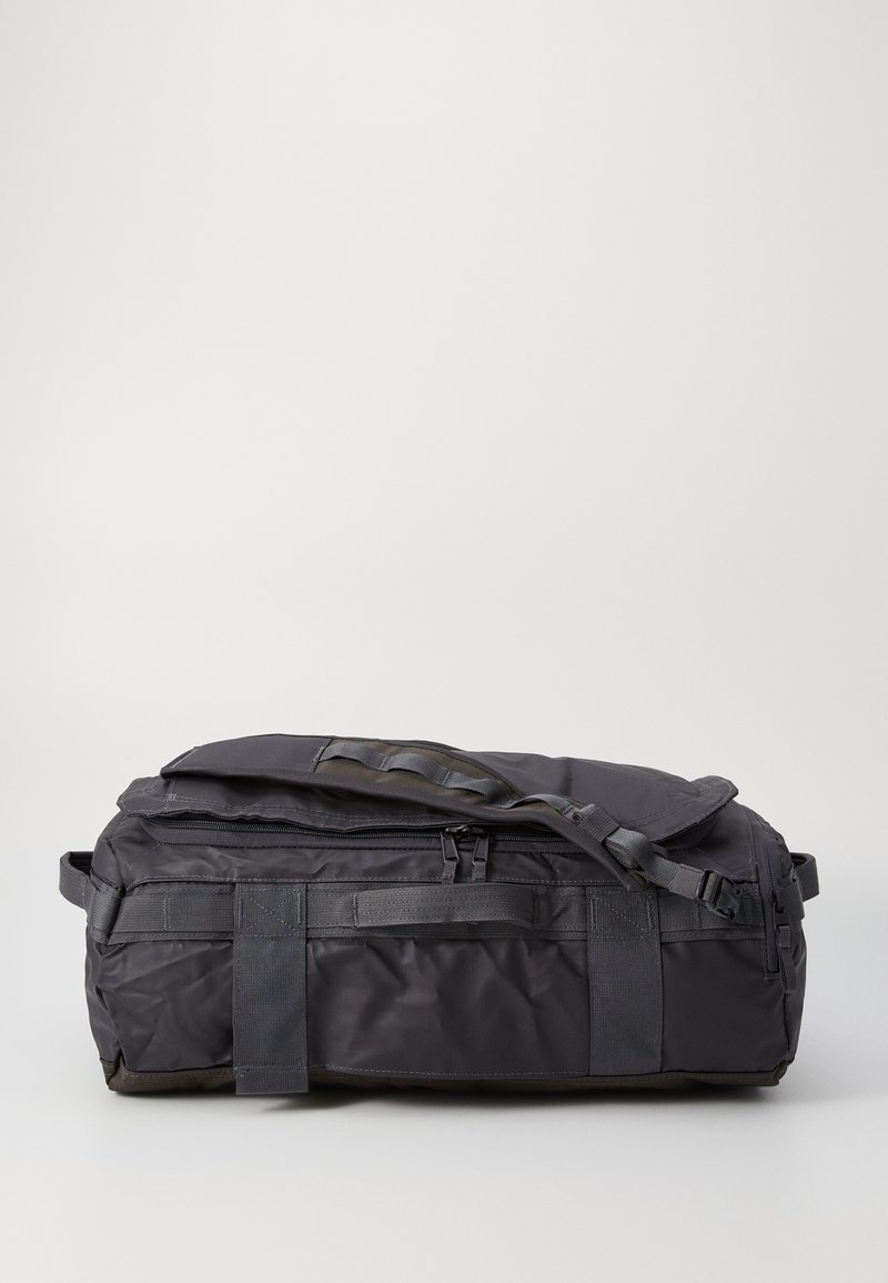 Black duffel bag made of durable nylon, featuring a zippered top closure, flat handle, and adjustable shoulder strap with webbing accents.