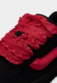 Baskets noires avec lacets en satin rouge froncés, tissu texturé et une bande d'accent rouge. Semelle épaisse en caoutchouc avec détail de crampons à motif.