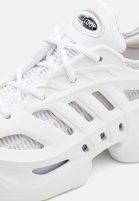 Valkoiset urheilukengät, joissa on verkko-yläosa ja kumiset yksityiskohdat. Ominaisuuksiin kuuluvat tuuletusaukot, nauhoitusjärjestelmä ja pyöreät pohjat.