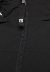 Svart jacka med en slät textur, hel dragkedja och en liten logotyp på dragkedjehandtaget. Designen är minimalistisk med rena linjer.