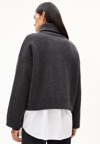 Donkergrijze oversized trui met een hoge kraag en verlaagde schouders, gemaakt van zachte stof, gelaagd over een wit shirt voor contrast.