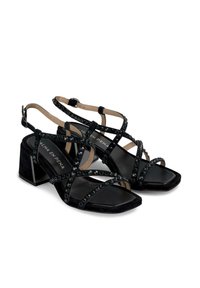 Schwarze Wildleder-Sandalen mit Blockabsatz, die mit kreuzförmigen Riemen und runden schwarzen Akzenten verziert sind. Design mit quadrater Zehenpartie und verstellbaren Fesselriemchen.