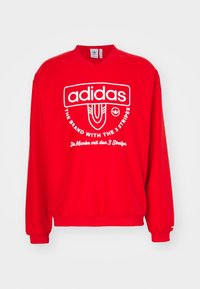 Red sweatshirt with long sleeves, v-neck design, featuring prominent white adidas logo and text. Soft texture, elastic cuffs and hem.