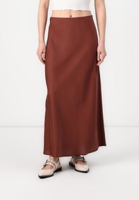 Brun, flytende maxi skjørt laget av glatt stoff, med høy midje og subtil drapering. Kombinert med lyse, flate sko.