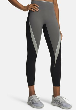 Vrouw draagt zwarte en grijze legging met hoge taille met lichtgrijze diagonale strepen en witte sportschoenen, staand met één hand op haar heup.