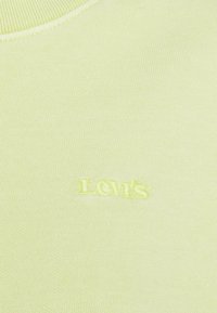 T-shirt en coton jaune pâle avec un col rond et le logo "Levi's" en relief cousu avec un fil jaune assorti. Texture lisse, coupe ajustée.