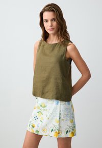 Top in lino verde oliva con scollatura tonda, abbinato a una gonna bianca con modelli a limone e floreali, accentuata da disegni blu.