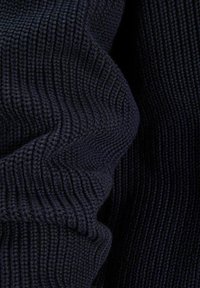 Laivastonsininen neulottu kangas, jossa on ribbikuvio ja pystysuorat raidat, näyttää pehmeältä. Joustavuus näkyy kankaan valahtelussa.