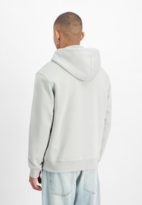 Gai pelēks kapuces krekls, izgatavots no mīksta auduma, ar brīvu griezumu, ribotām piedurknēm un apakšmalu. Aizmugurē ir minimālas detaļas.