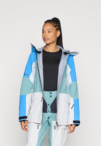 GORE-TEX jakna s višebojnim dizajnom u plavim, sivozelenim i zelenim panelima; veliki kapuljača; prednji zatvarač; više džepova; vodootporni materijal.