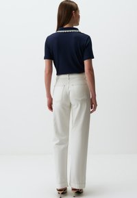 Polo shirt côtelé marine avec un col festonn�é, associé à un pantalon blanc taille haute. Texture lisse et coupe décontractée.