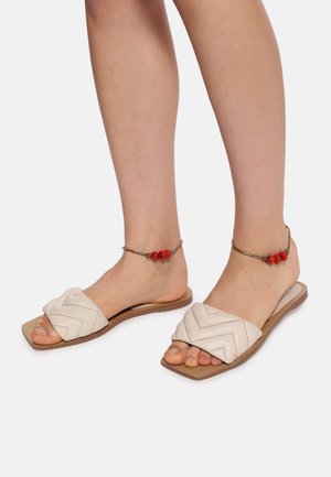 Lette beige slide sandaler med vævet chevronmønster, flad sål og ankelarmbånd med røde perler. Glat lædermateriale.