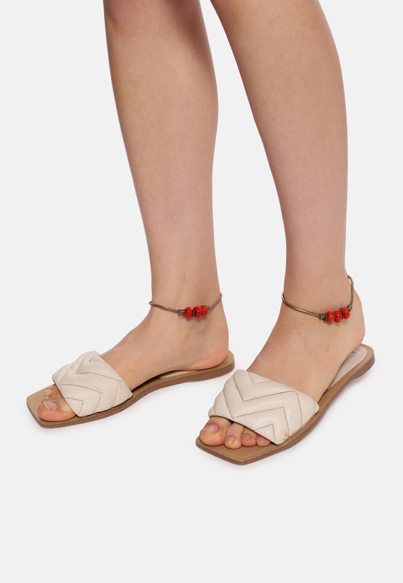 Lette beige slide sandaler med vævet chevronmønster, flad sål og ankelarmbånd med røde perler. Glat lædermateriale.