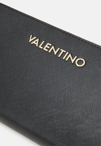 Črno teksturirano usnjeno denarnico z zlatim logotipom "Valentino" spredaj, elegantne pravokotne oblike in gladkimi robovi.