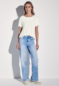 Hvid kortærmet t-shirt kombineret med lyseblå lige ben jeans og beige sneakers, med en afslappet pasform og glat stofstruktur.