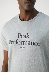 Grå bomull t-skjorte med rund hals, korte ermer og et svart grafisk trykk som leser "Peak Performance Est. 1986" på fronten.