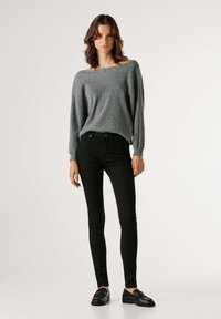 Pilkas megztinis su plačiu iškirpimu, juodi laisvi džinsai, ir juodi tekstūruoti batai. Minkšta medžiaga, laisvas kirpimas, ir kasdienis stilius.