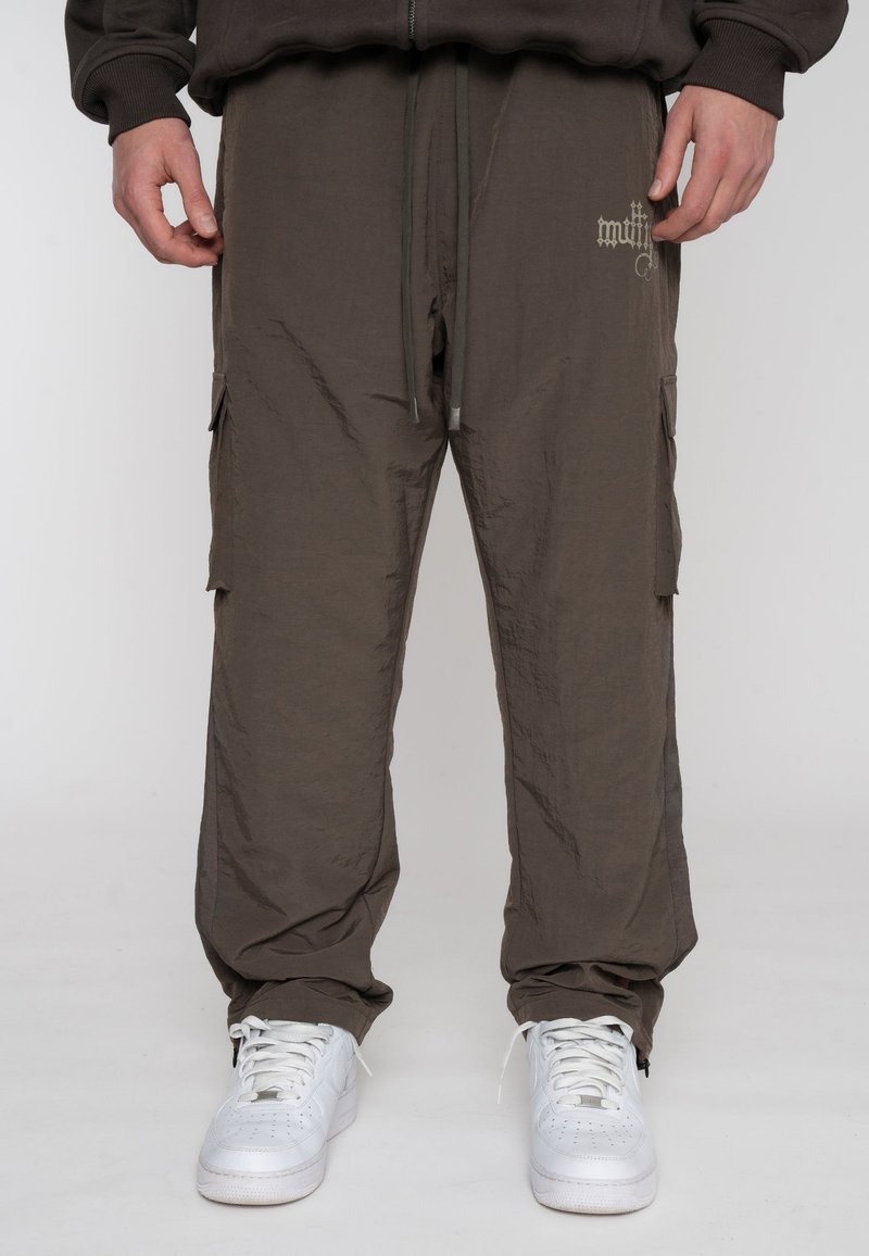 Cargo-broek in een lichtbruine, gestructureerde stof met zijzakken en een trekkoord in de taille, gedragen met witte sneakers.