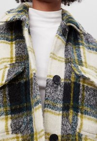 Skjortjacka i ullblandning med rutmönster i kräm, grått, gult och teal. Har stora knappar, krage och fickdetaljer. Mjuk och texturerad tyg.
