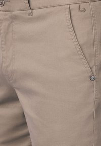 Beżowe spodnie bawełniane o gładkiej fakturze, z małym logo na guzie oraz starannie wykończonymi kieszeniami i paskiem.