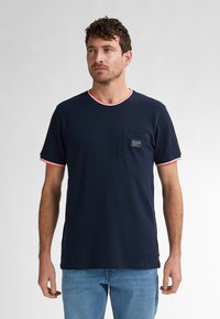 Mörkblå bomull t-shirt med rund hals, kontrasterande rosa kant, korta ärmar och en bröstficka med en etikett.