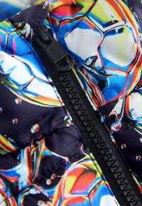 Gros plan d'une fermeture éclair noire sur un tissu coloré avec des motifs abstraits multicolores rappelant des gouttes d'eau et des reflets.