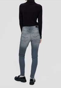 Vaqueros ajustados grises con bolsillos traseros, cintura alta y un sutil desgaste. Combinados con un suéter de cuello alto negro y zapatos plataforma negros.