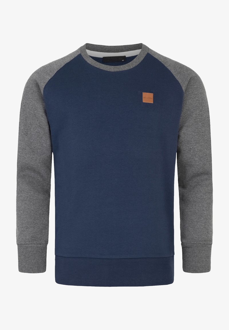 Marineblauer Pullover mit grauen Raglanärmeln, strukturiertem Stoff, gerippten Bündchen und Bund; mit einem kleinen braunen Lederpatch auf der Brust.
