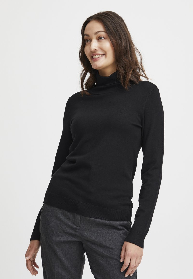 Maglione nero a maniche lunghe con collo alto e vestibilità slim. Tessuto morbido, polsini e orlo a coste. Abbinato a pantaloni grigi sartoriali.