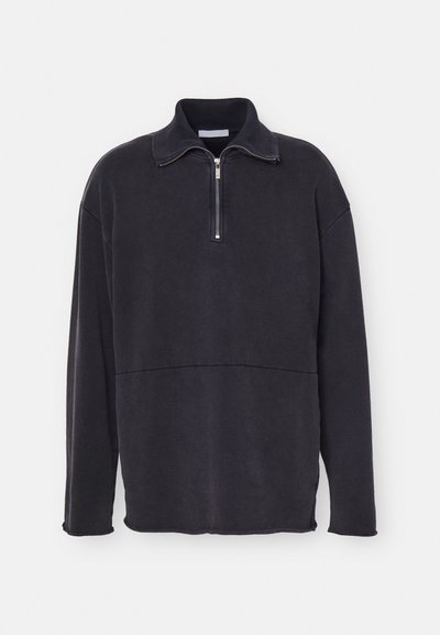 Tummanharmaa vetoketjukauluksellinen neule, ylipitkä muotoilu, teksturoitu kangas ja saumaan yksityiskohta rinnan kohdalla. Pitkät hihat, rento istuvuus.