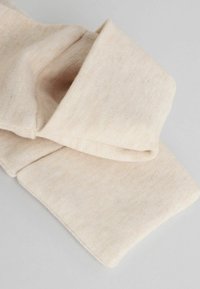 Bufanda de algodón en un suave color beige pálido con una textura lisa, que presenta un diseño plegado y sutiles variaciones en el tono.