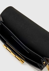Čierna kožená kabelka do ruky s hladkou textúrou, zlatými kovaniami, obdĺžnikovým tvarom a priestranným vnútrom s priehradkami na karty.