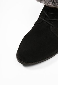 Bottine en daim noir avec bout arrondi, design à lacets et bordure en fausse fourrure en haut, avec une semelle en caoutchouc cousue.