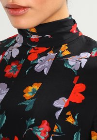 Schwarzer Stoff mit lebhaftem Blumenmuster in Rot, Orange und Lila. Verfügt über einen hohen Kragen und eine strukturierte Oberfläche, mit einem zentralen Nahtdetail.