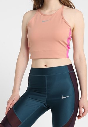 Frau trägt pfirsichfarbenes ärmelloses Crop-Top und türkisfarbene Leggings mit hoher Taille und dunkelvioletten Einsätzen, beide mit kleinen silbernen Nike-Logos.
