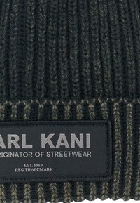 Black and olive green ribbed beanie with textured fabric. Features a rectangular gray label with "KARL KANI" and "ORIGINATOR OF STREETWEAR."