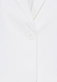 Un unique bouton blanc ferme le devant d'un blazer blanc avec un col à revers cranté.