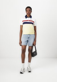 Polo shirt med lynlås, med gule, hvide, røde og marineblå striber. Parret med denimshorts, sorte håndtaske og sølvfarvede sneakers.