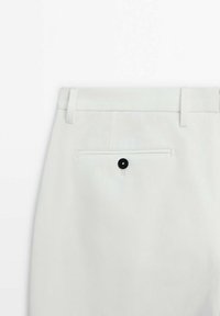 Pantaloni bianchi caratterizzati da un design pulito, tasca welt sul retro con bottone nero e passanti per la cintura. Il tessuto ha una superficie liscia e sottile.