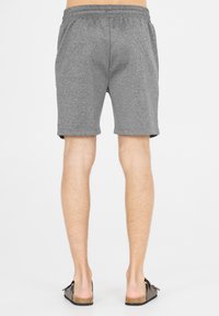 Grijze sportshorts met een elastische tailleband, een gladde textuur en een knielange snit, gecombineerd met donkere instapsandalen.