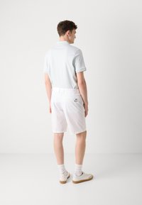 Un polo bleu clair et un short blanc, mettant en avant une texture lisse, avec un détail de logo sur la poche arrière, le tout assorti à des baskets blanches.