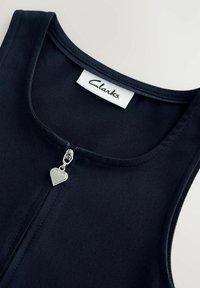 Schwarze Stoffweste mit einem silbernen herzförmigen Reißverschluss und einem weißen "Clarks"-Label am Halsausschnitt. Glatte Textur, ärmelloses Design.