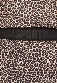 Tissu à imprimé léopard beige et marron avec une ceinture élastique noire arborant des lettres en relief indiquant "SPORT". Texture lisse.
