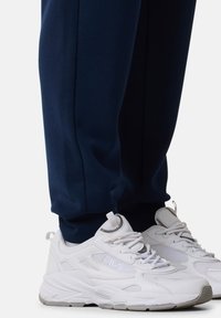 Weiße Sportschuhe mit Netzeinsätzen und einer strukturierten Gummisohle, getragen mit navyblauen Stretchhosen mit tailliertem Design und elastischen Bündchen.