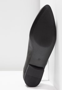 Semelle d'une chaussure noire à bout pointu avec zone d'adhérence texturée et petit talon bloc, taille indiquée 37, sur un fond blanc en coin.