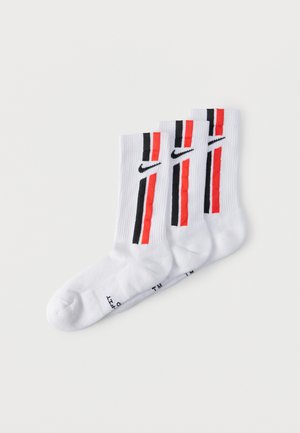 Trois chaussettes montantes blanches Nike avec des rayures verticales noires et rouges et des logos Nike swoosh noirs de chaque côté.