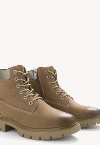 Ruskeat nahkabootsit, joissa on nauhakiinnitys, pehmustettu kaulus ja sivu vetoketju. Ominaisuuksiin kuuluu kuormittava, teksturoitu pohja ja kontrastiväriset ompeleet.